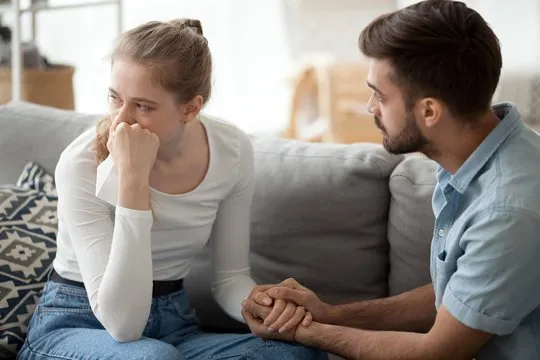 A couple sitting apart on a couch, upset