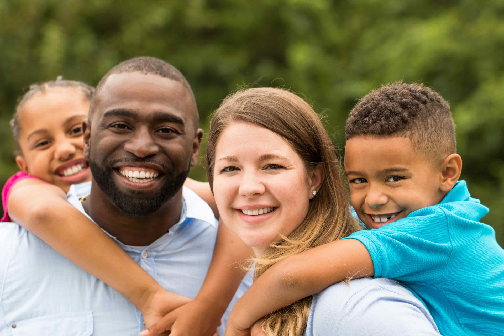 A smiling family of four hugging outdoors