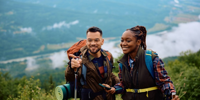 Two hikers smiling together on a mountain trail overlooking a green valley