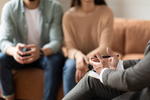 A therapist holding a clipboard and pen while speaking with a couple seated on a couch